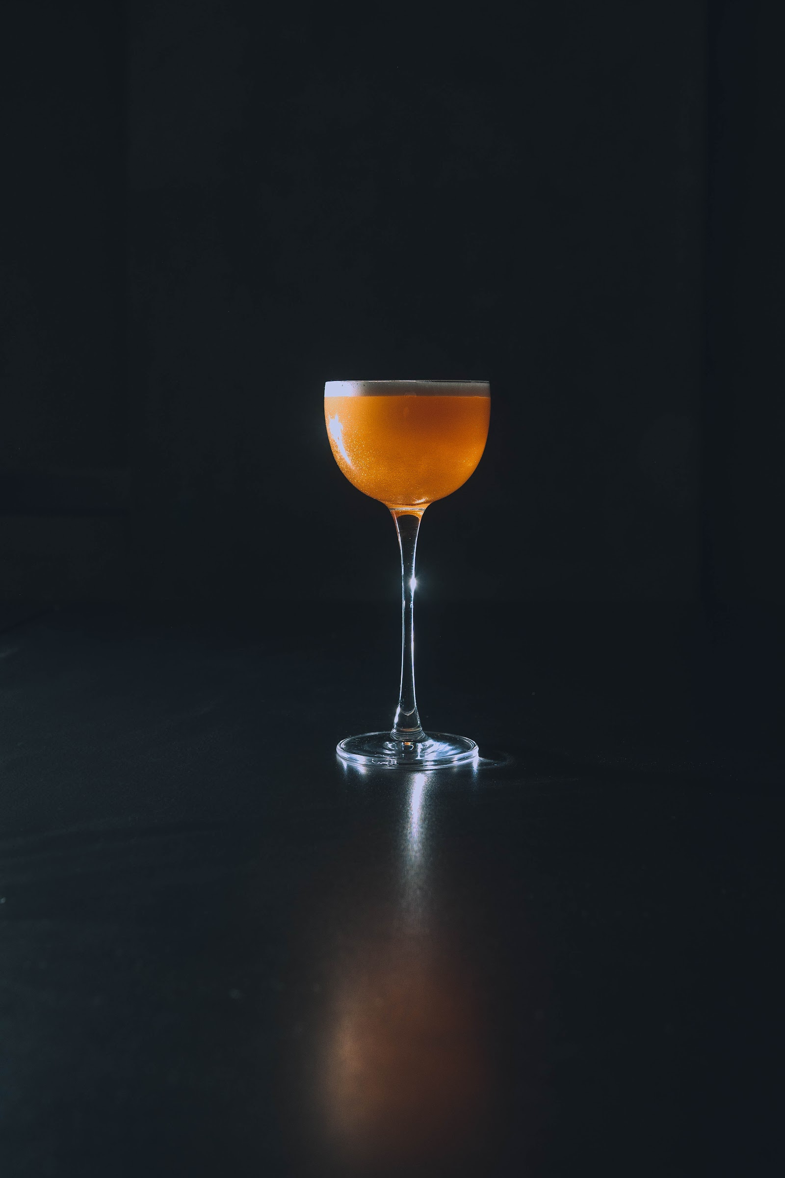 Coupe cocktail with amber liquid on dark surface at KINKI Cocktail Club Malasaña