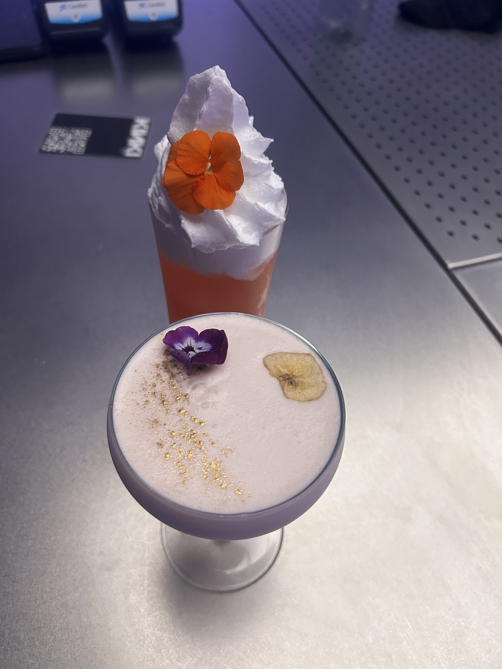 Two KINKI cocktails side by side on a dark bar top, warm candlelit atmosphere