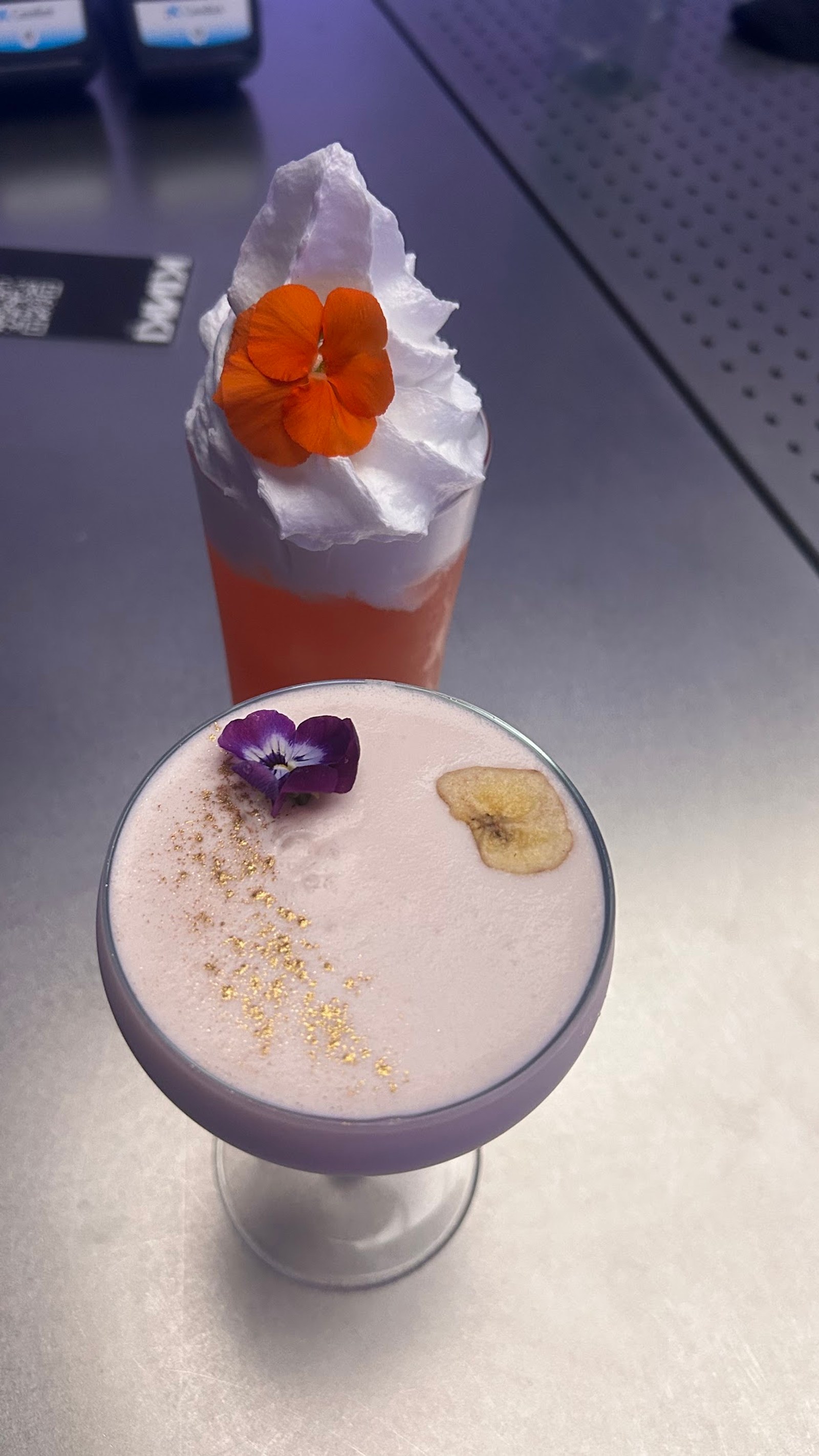 Two signature cocktails with floral garnishes on a dark counter at KINKI Cocktail Club