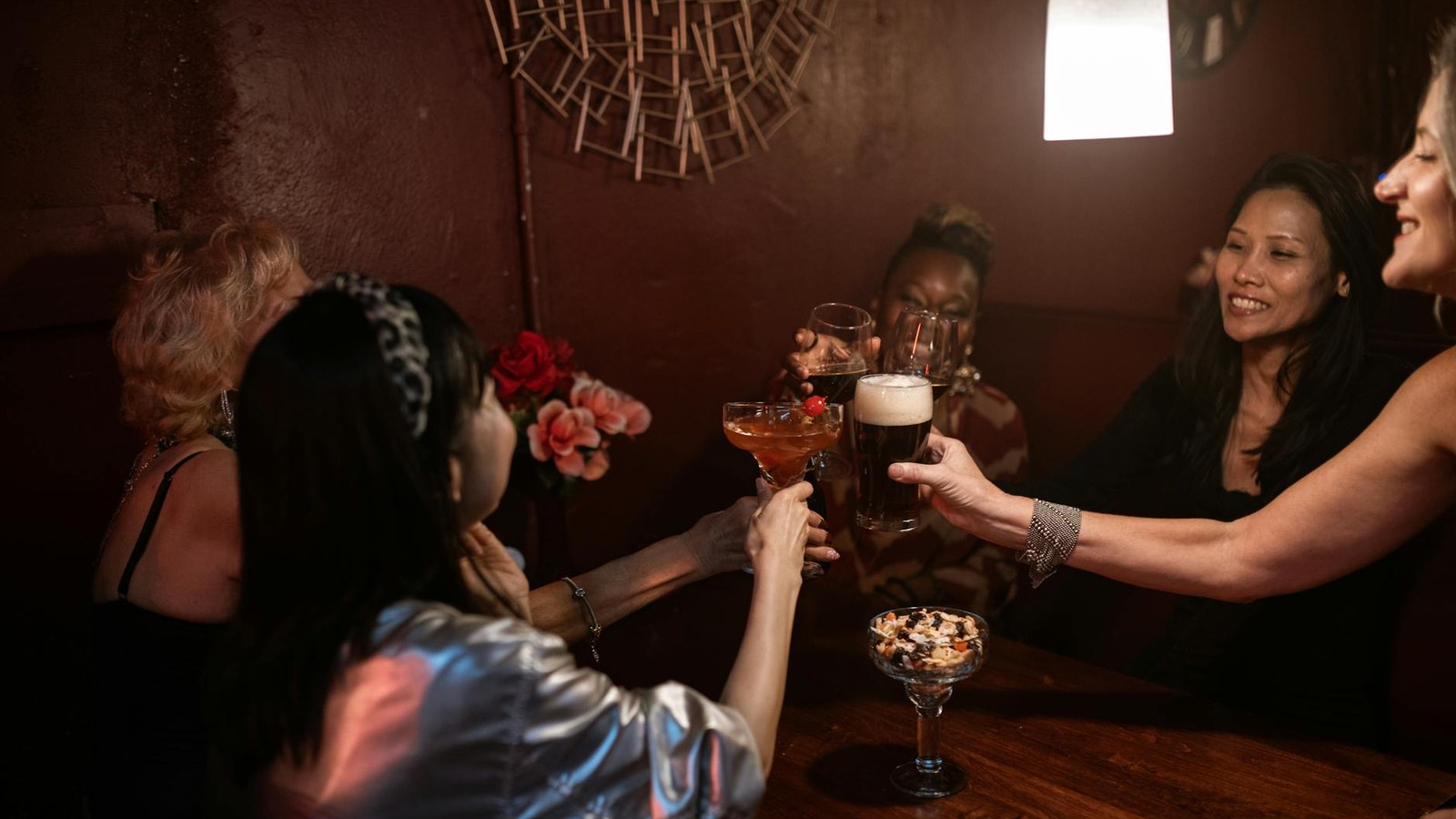 Group celebrating at a cocktail bar, glasses raised, dark ambient lighting